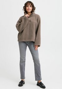 Brun fleece pullover med halv-zip krave, lange ærmer og en blød tekstur. Parret med grå lige ben jeans og sorte loafers.