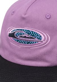 Purple cotton cap with black brim, featuring an embroidered logo with blue and black details. Textured fabric with stitched accents.