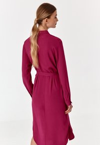 Fuktsia värvi pikkade käistega kleit, millel on vööga talje, nööbitavad varrukad ja sirge lõige, klassikalise krae ja külgaukudega.