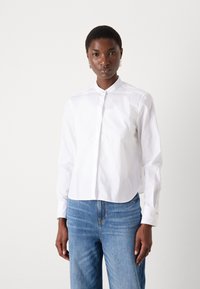 Witte button-up overhemd met een kraag, lange mouwen en een gladde textuur, gecombineerd met lichtblauwe denim jeans. Eenvoudig, schoon ontwerp.