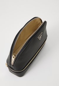 Borsa in pelle nera con hardware dorato e superficie testurizzata. L'apertura con zip superiore rivela una fodera interna beige. Presenta un dettaglio con logo.