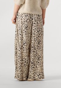 Leopard print wide-leg pants in beige, featuring soft, pleated fabric with a glossy finish, paired with a cream textured sweater.