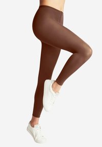 Leggings marroni realizzati in materiale elasticizzato, design aderente e texture liscia, abbinati a sneakers bianche.