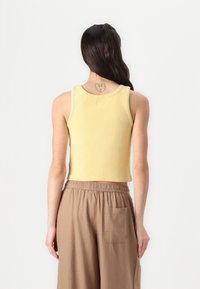 Yellow ribbed tank top with a fitted design, featuring a round neckline and sleeveless cut, paired with brown elastic-waist pants.