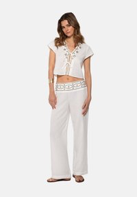 Top corto de lino blanco con bordados decorativos y lazos en el escote; pantalones anchos de lino a juego con una cinturilla bordada.