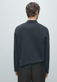 Czarna koszula z długim rękawem i kołnierzykiem, o gładkiej teksturze i luźnym kroju, widziana od tyłu z minimalistycznym wzornictwem.