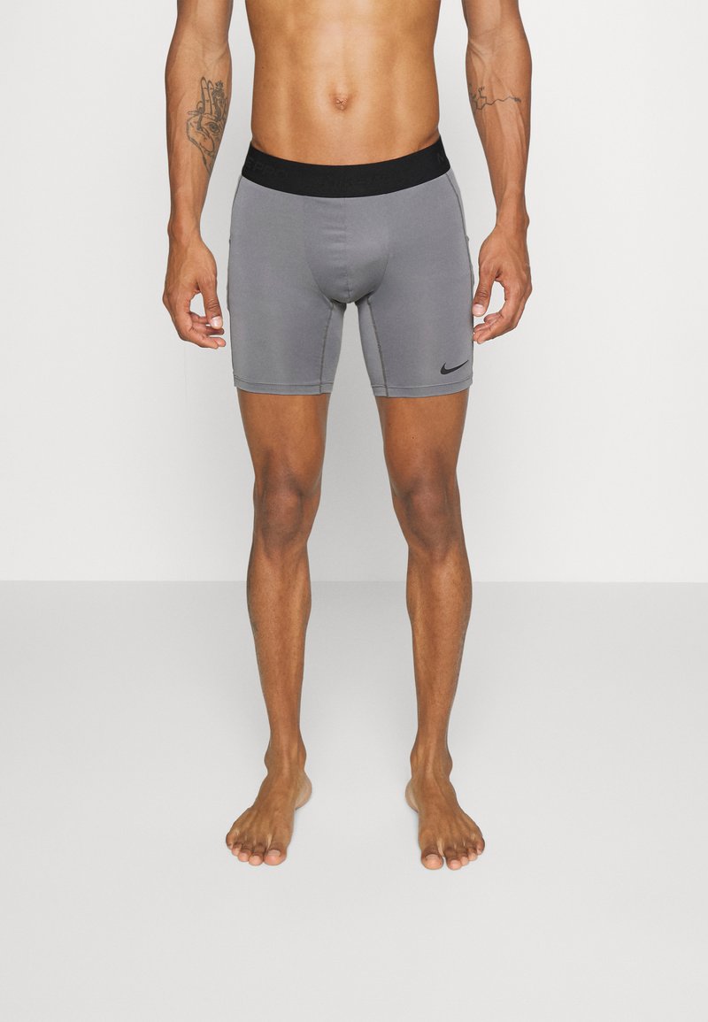 Grå atletiska shorts med ett svart elastiskt midjeband som har en logotyp. Slät textur, knälång design, lämplig för aktiv klädsel.