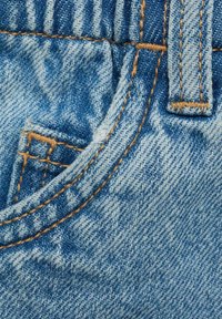 Sininen farkkukangas, jossa on haalistunut tekstuuri, etutasku ja kontrastiväriset oranssit tikit saumoissa ja vyötäröllä.