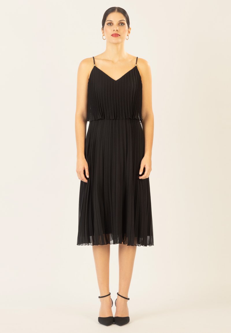 Schwarzes, plissiertes Kleid mit verstellbaren Spaghettiträgern und taillierter Taille. Durchsichtiger Saum, kombiniert mit schwarzen spitzen Schuhen.