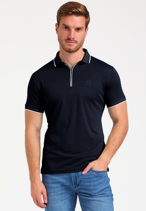 Polo de color navy con cuello con cremallera, ribete blanco en el cuello y las mangas, diseño ajustado, hecho de una tela suave, y un pequeño logo en el pecho.
