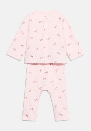 Σετ πιτζάμες μωρού σε ανοιχτό ροζ χρώμα με μακριά μανίκια και μικρά κόκκινα ανθισμένα σχέδια, με κουμπιά τύπου σναπ στο μπροστινό μέρος του πάνω μέρους.