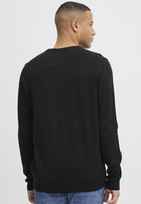 Maglione nero con maniche lunghe, scollatura rotonda e polsini a coste. Realizzato in materiale morbido con una texture semplice. Vista posteriore, indossato su jeans blu.