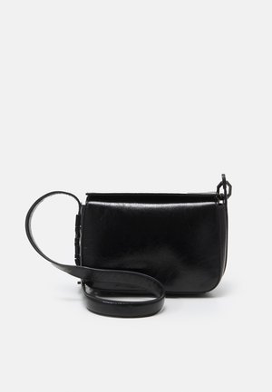 Petit sac en cuir noir en bandoulière avec un fond incurvé, fermeture rabat et une sangle ajustable enroulée sur un fond blanc.