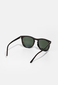 Ochelari de soare tortoise maro cu lentile verzi. Formă rotundă, textură netedă și brațe subțiri negre cu detalii discrete de branding.