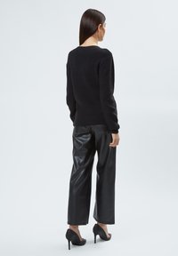 Zwart gebreid sweatshirt met geribbelde manchetten, gecombineerd met zwarte leren wijde broek en zwarte hoge hakken, gezien vanuit de achterkant.