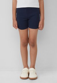 Marineblaue ribbelige Stoffshorts mit einem taillierten Design und einem glatten Saum. Kombiniert mit weißen Sneakers mit einer Gummisohle und Klettverschluss.