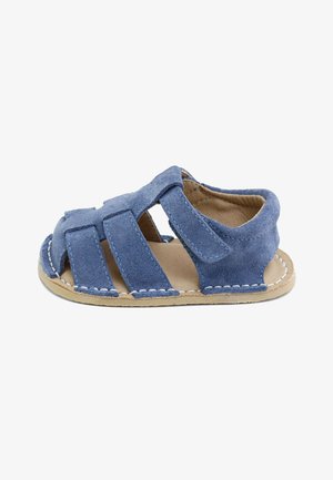 Sandalia azul de ante para niño pequeño, con punta abierta, tres tiras y cierre de velcro sobre una suela marrón claro con costuras blancas.