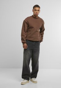 Bruine trui met ronde hals, gecombineerd met losse, donkere denim jeans en lichte sneakers. Gemaakt van katoen met een relaxte pasvorm en zichtbare stiksels.