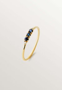 Anillo de oro con cinco piedras preciosas azul oscuro y dos pequeños acentos claros, con una banda delgada que se estrecha hacia la parte posterior.