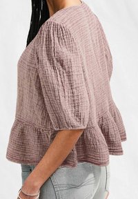 Puff-sleeve top in soft, textured mauve fabric with a tiered peplum hem. Features slight gathering at shoulders and small raised dots throughout.