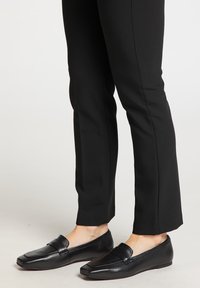 Sorte læder loafers båret med sorte straight-leg bukser på en lys gulvbagtgrund.