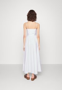 Langes, lilafarbenes Kleid mit dünnen Trägern, einem gerafften Rücken und einer fließenden Silhouette. Kombiniert mit braunen Plateausandalen. Minimalistisches Design.