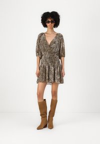 Abito con stampa leopardata, scollo a V profondo, maniche a sbuffo e vita smock; abbinato a stivali al ginocchio in suede color cammello.