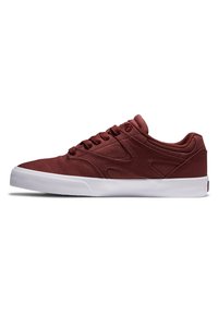 Rote Canvas-Skate-Schuhe mit einer flachen weißen Gummisohle, ausgestattet mit einer geschlossenen Schnürung, gepolstertem Kragen und strukturierten Details an den Seitenpaneelen.