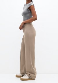 Haut à manches courtes côtelé gris clair associé à un pantalon beige à jambes larges et des baskets blanches avec des accents bleu marine. Textures lisses et coupe ajustée.