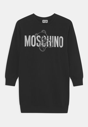 Czarna sukienka z długim rękawem z napisem "MOSCHINO" na wysokości klatki piersiowej oraz konturami misia, które nachodzą na litery.