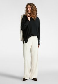 Zwart langslavend top met een losse pasvorm, gecombineerd met off-white wijde broekspijpen. De outfit heeft een casual, hedendaags ontwerp.