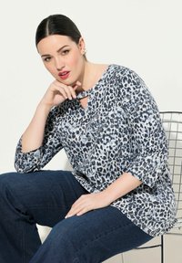 Niebieska i biała bluzka w wzór panterki z dekoltem w kształcie łezki, rękawami 3/4 i luźnym krojem, w połączeniu z ciemnoniebieskimi dżinsami.