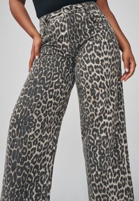 Pantalon à larges jambes imprimé léopard en beige clair et noir, avec une taille haute, une fermeture à boutons et un tissu doux et texturé.