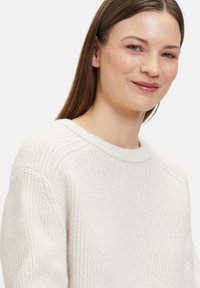 Strickpullover in cremigem Weiß mit einem gerippten Ausschnitt und strukturiertem Muster. Verfügt über eine lockere Passform und überschnittene Schulternähte.