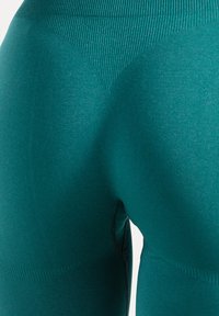 Leggings taille haute couleur sarcelle en tissu extensible. Possèdent une ceinture côtelée et une texture lisse avec un design profilé pour un ajustement parfait.