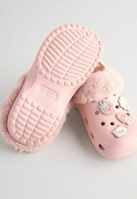Sabots roses duveteux avec des charms décoratifs, semelles en caoutchouc texturé, trous de ventilation et un doux bord en fourrure autour de l'ouverture.