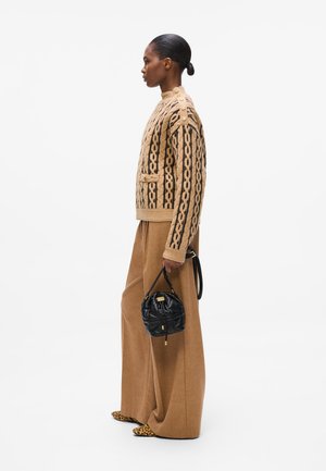Tan gebreid sweater met zwart patroon, voorzien van zijknopen; brede bruine broek; zwarte ronde tas; schoenen met dierenprint.