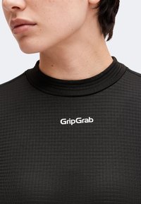 Gros plan d'une personne portant une chemise noire texturée avec un col haut et un logo blanc "GripGrab" sur la poitrine.