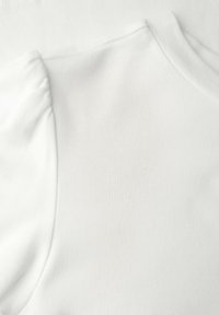 Haut blanc à manches courtes en coton doux et lisse. Présente un col rond et un détail froncé à l'épaule pour varier les textures.