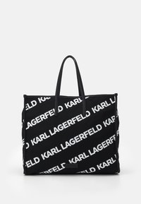 Svart tote-väska med vit "KARL LAGERFELD" text tryckt diagonalt. Har långa svarta handtag och en slitstark tygkonstruktion.