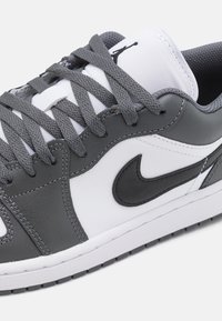 Baskets basses blanches et grises avec lacets gris, logo Nike Swoosh noir, et logo Jumpman noir sur la languette blanche.