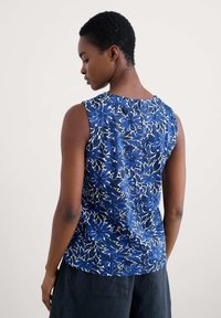 Ärmlös topp i blåblommigt mönster på vit bakgrund. Mjuk tygkvalitet med rund halsringning; enfärgad baksida; slutar strax ovanför midjan.