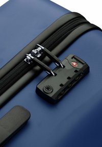 Valigia blu con zip, dotata di lucchetto TSA nero che tiene bloccati due cursori della zip su una superficie in tessuto texturizzato.