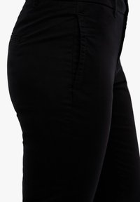 Pantalon noir en mélange de coton avec une texture lisse, doté de poches latérales et d'une coupe ajustée, présenté en gros plan de profil.