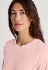 Light pink long-sleeve top with a rounded neckline. The fabric appears smooth and soft, featuring a simple, unembellished design.