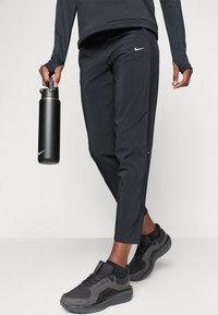 Nike svarte treningsbukser med smale ben, med sidelommer, kombinert med svarte sko og holder en svart vannflaske.