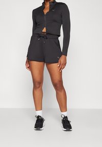 Svart atletisk klädsel bestående av en zip-up långärmad topp och shorts med dragsko. Materialet verkar lätt och andas, med logotypdetaljer.