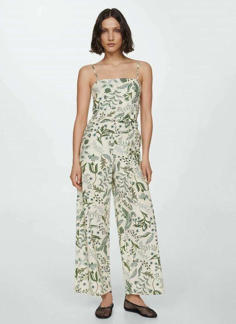 Combinaison florale en tissu crème clair ; dotée de bretelles spaghetti, de jambes larges et d'un imprimé botanique vert partout. Chaussures plates texturées noires.