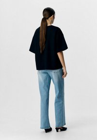 Zwarte oversized t-shirt met korte mouwen, gecombineerd met lichtblauwe rechte jeans en zwarte hakken. Eenvoudige, ontspannen silhouet.