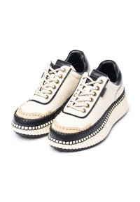 Sneaker platform crema e nere con suole spesse a coste, lacci frontali e dettaglio in beige attorno all'area delle punte.